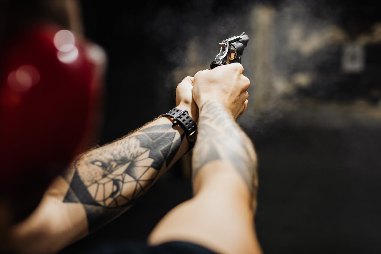 portfolio-05 Close-up of tattooed arms aiming and firing a revolver in an indoor shooting range.