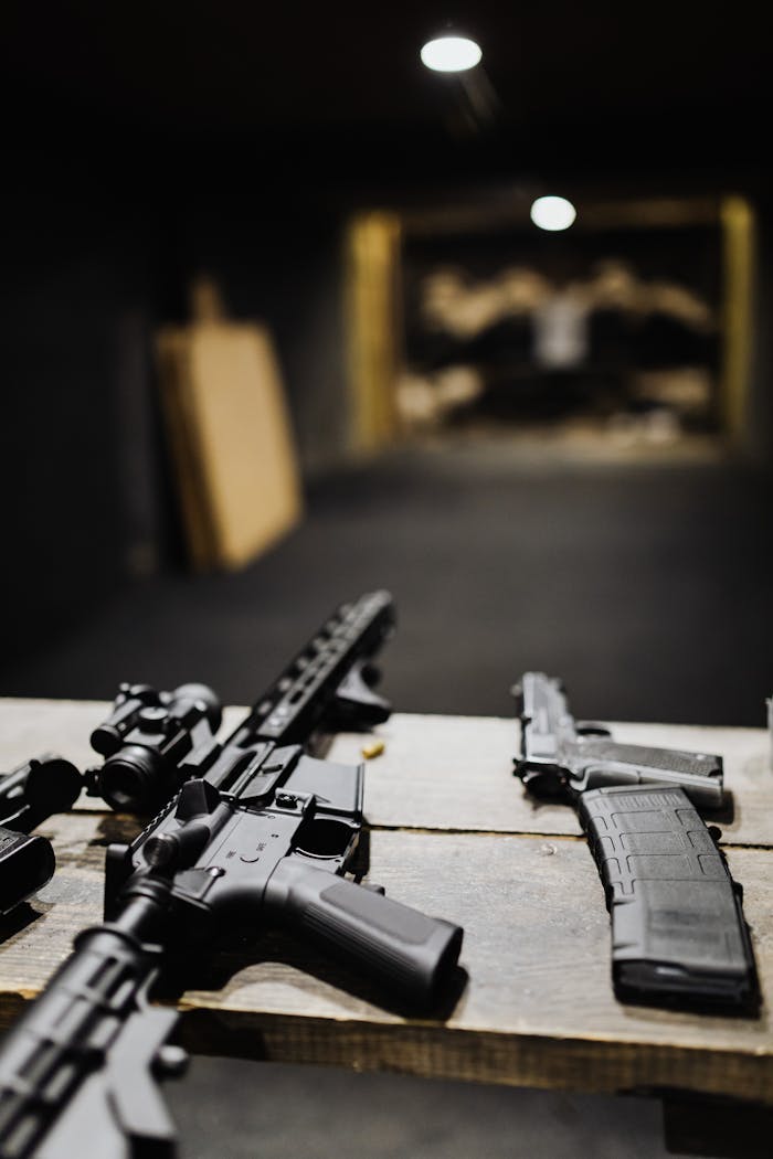 why-choose-us Assault rifles and handguns on a table at an indoor shooting range.